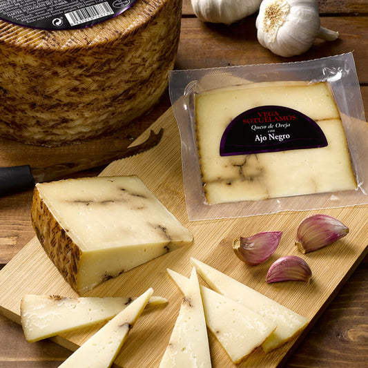 Round wheel of cheese with packaging and sliced pieces on a wooden board, surrounded by garlic.